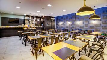 A restaurant interior with multiple tables and chairs, a bar area, and a wall with acoustic panels.