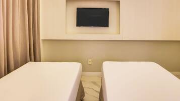 Habitación de hotel con dos camas individuales, un televisor de pantalla plana montado en la pared y una cortina a la izquierda.