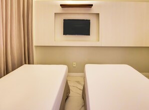 A hotel room with two single beds, a flat-screen TV mounted on the wall, and a curtain on the left.