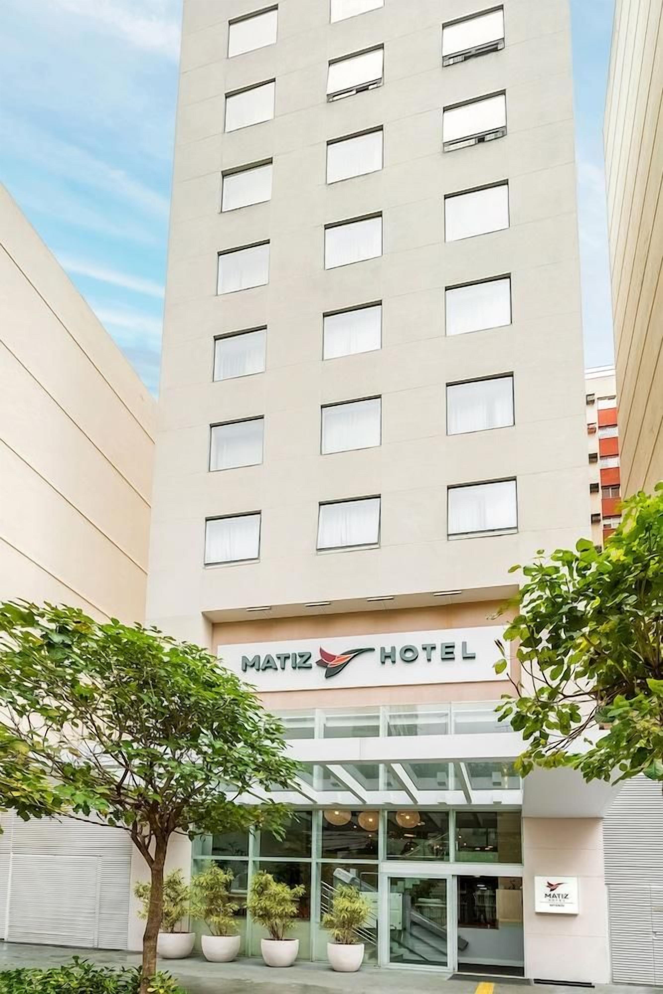 Un moderno edificio hotelero con fachada plana, múltiples ventanas y un letrero que dice 'MATIZ HOTEL' en la entrada.