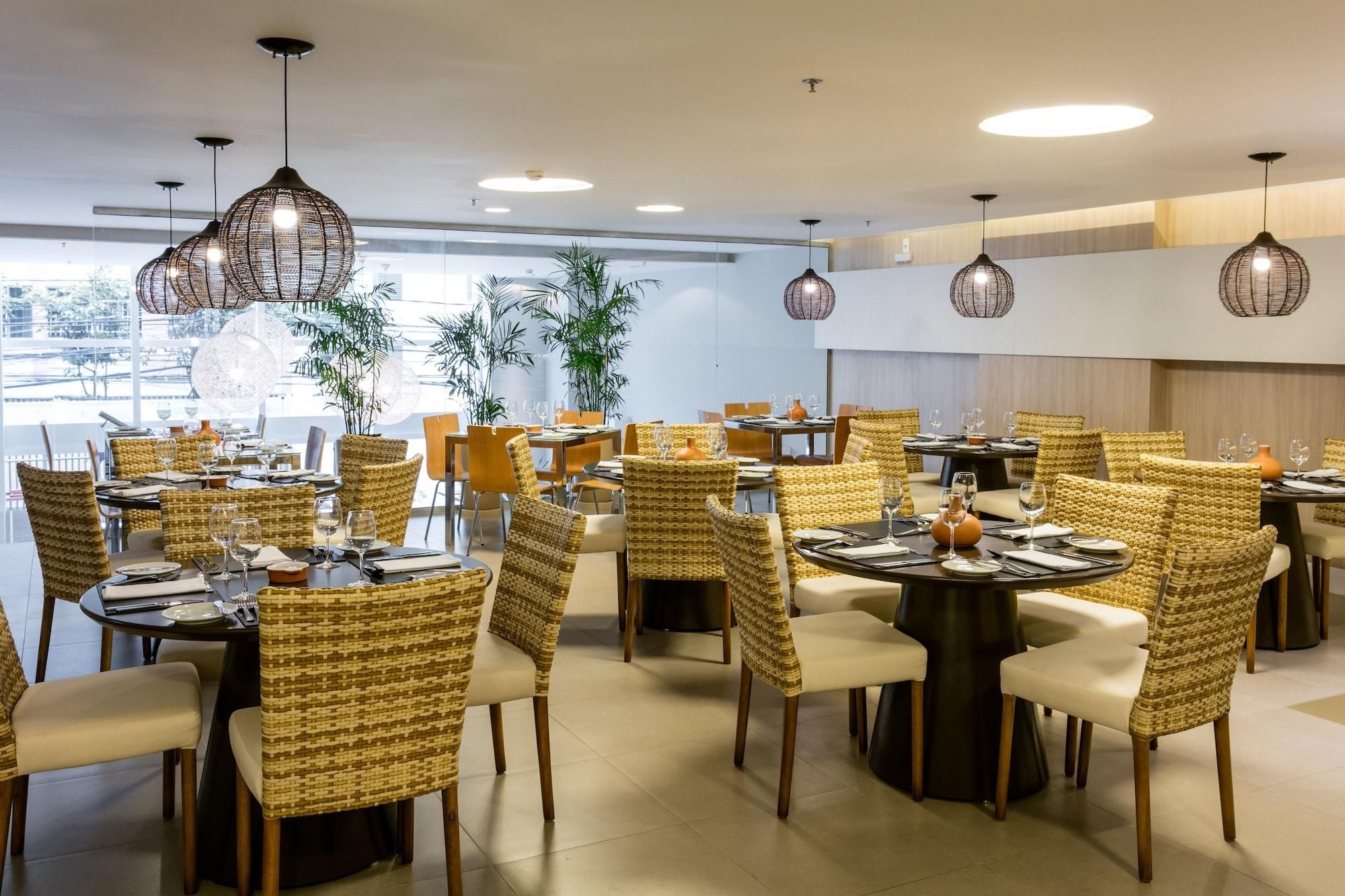 A restaurant with round tables, wicker chairs, and hanging light fixtures.