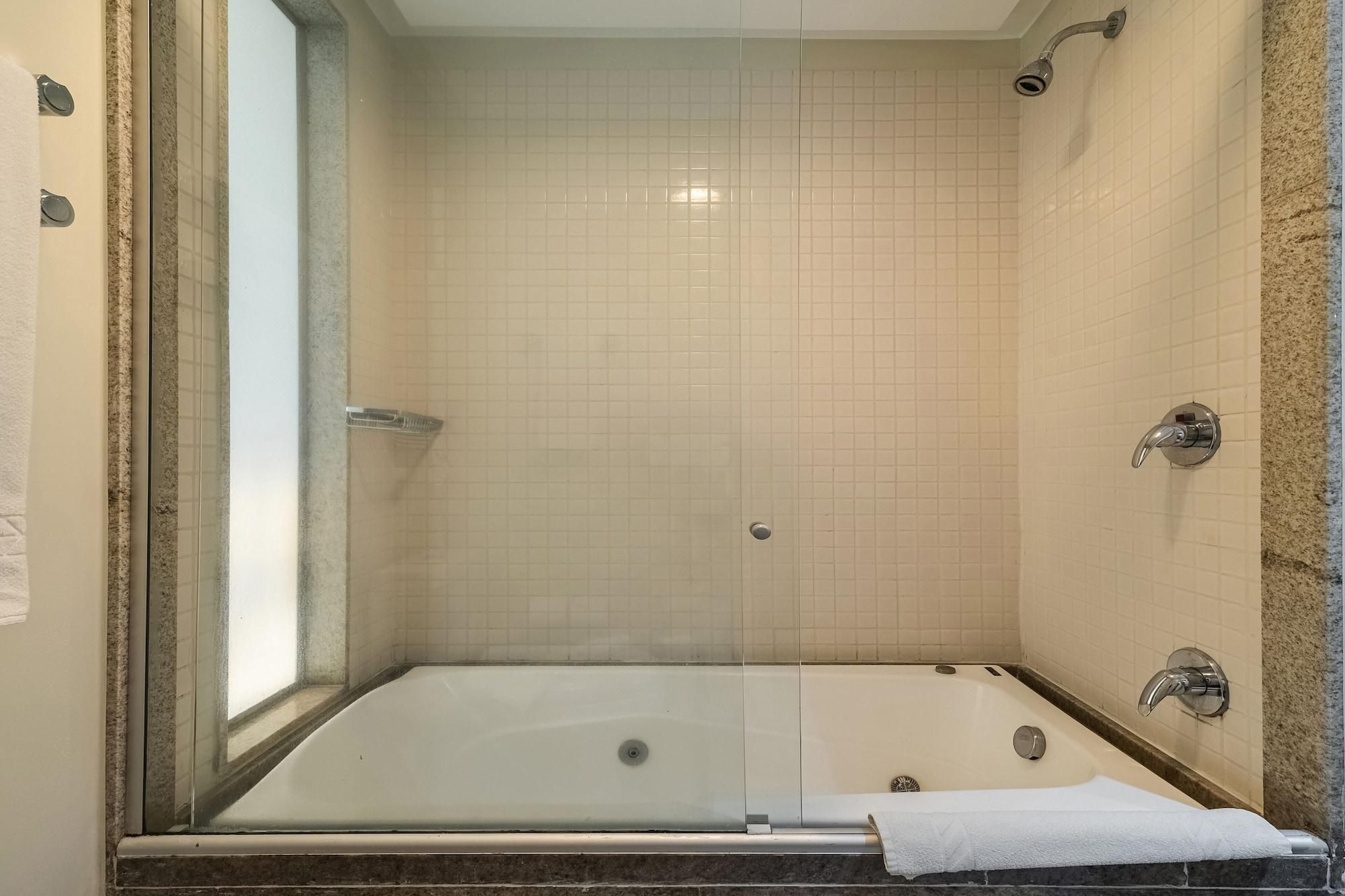 Ducha a nivel con puerta de vidrio, paredes de azulejos y una bañera con una toalla.