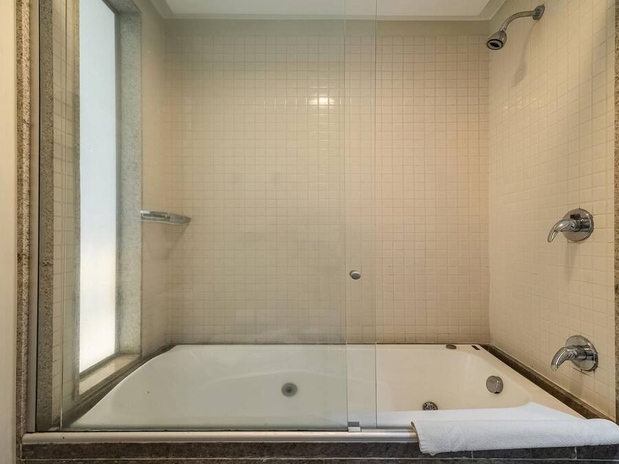 Ducha a nivel con puerta de vidrio, paredes de azulejos y una bañera con una toalla.