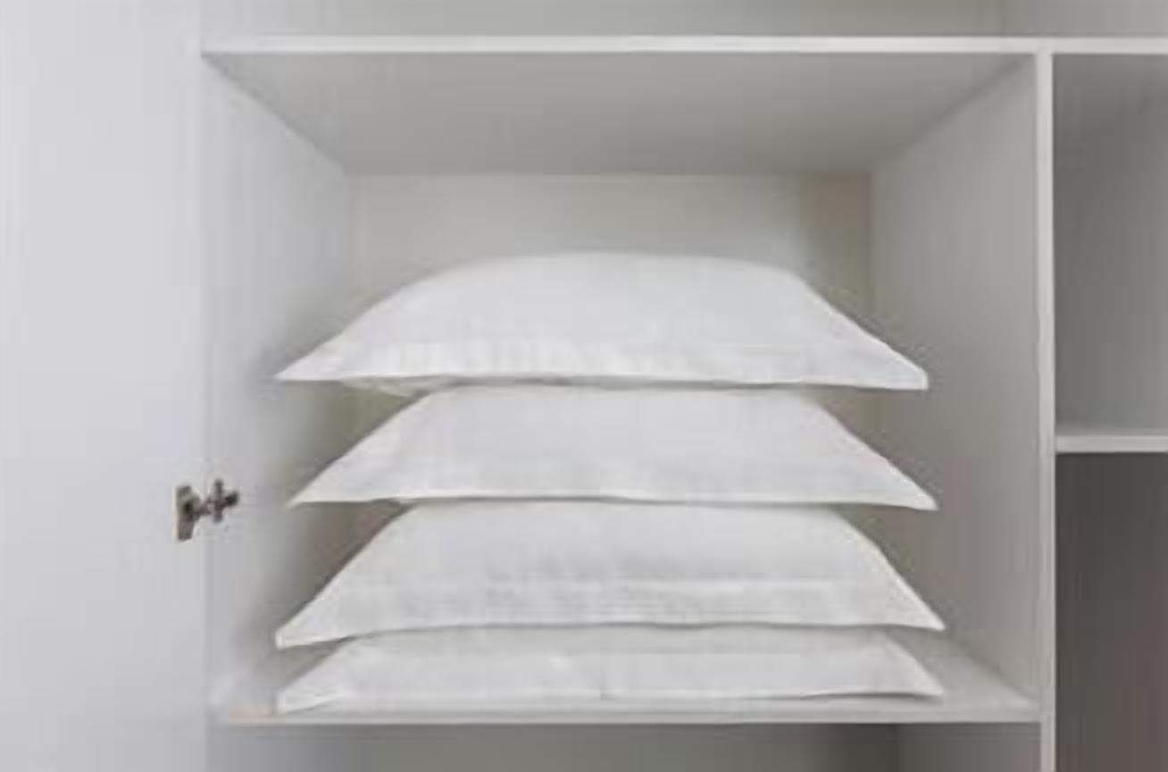 Um armário branco com várias prateleiras, cada uma contendo roupas de cama brancas dobradas.