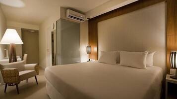 Quarto de hotel com uma cama grande, uma cadeira, uma escrivaninha e um ar condicionado.