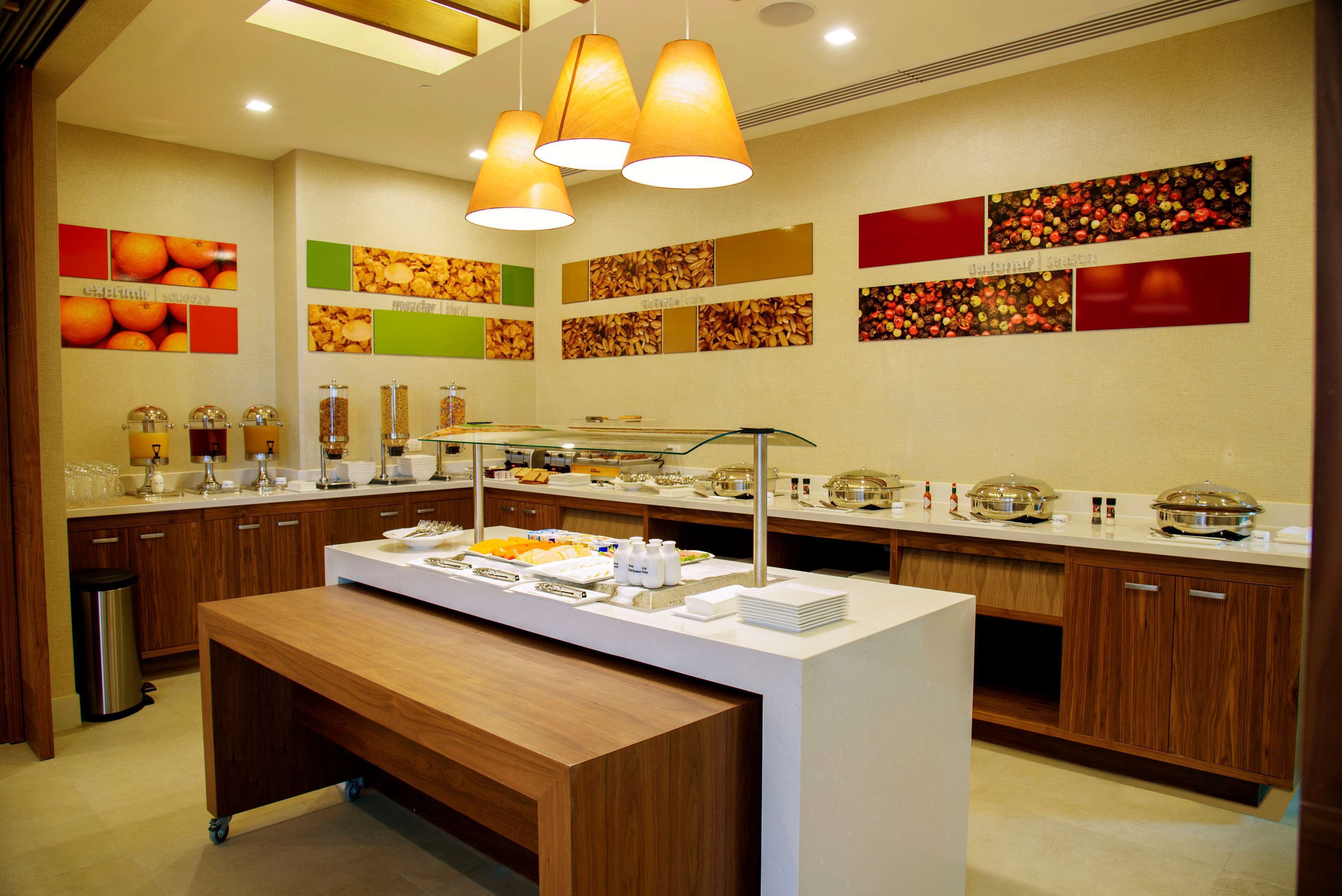 A buffet setup with a variety of food items and beverages, a wooden bench, and a wall decorated with fruit and nut images.