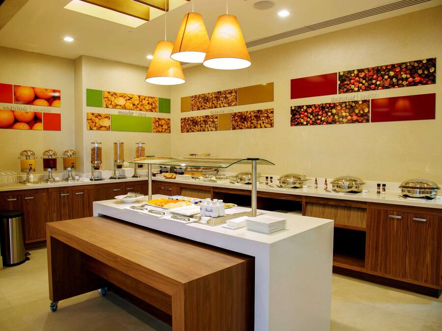 A buffet setup with a variety of food items and beverages, a wooden bench, and a wall decorated with fruit and nut images.