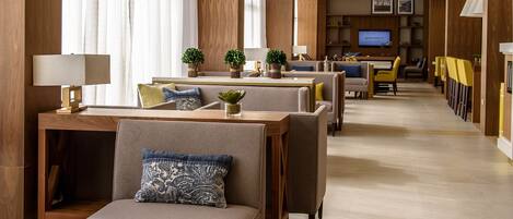 Un moderno vestíbulo de hotel con un área de estar central, un televisor y un diseño de techo de madera.