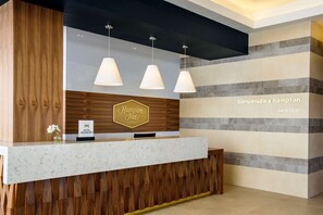A hotel reception desk with a wooden panel design, a marble countertop, and three pendant lights. - Hampton Inn by Hilton Piedras Negras (Piedras Negras)