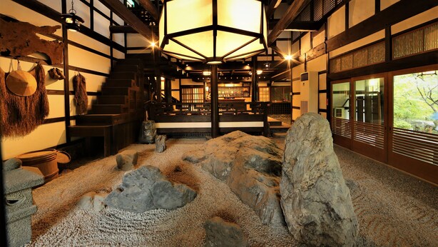 A traditional Japanese interior with tatami flooring, a central hexagonal lantern, and a view of a garden through sliding doors. - Momijiya Bekkan Kawanoiori (Kyoto)