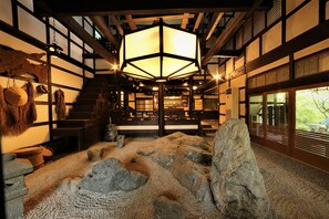 A traditional Japanese interior with tatami flooring, a central hexagonal lantern, and a view of a garden through sliding doors. - Momijiya Bekkan Kawanoiori (Kyoto)