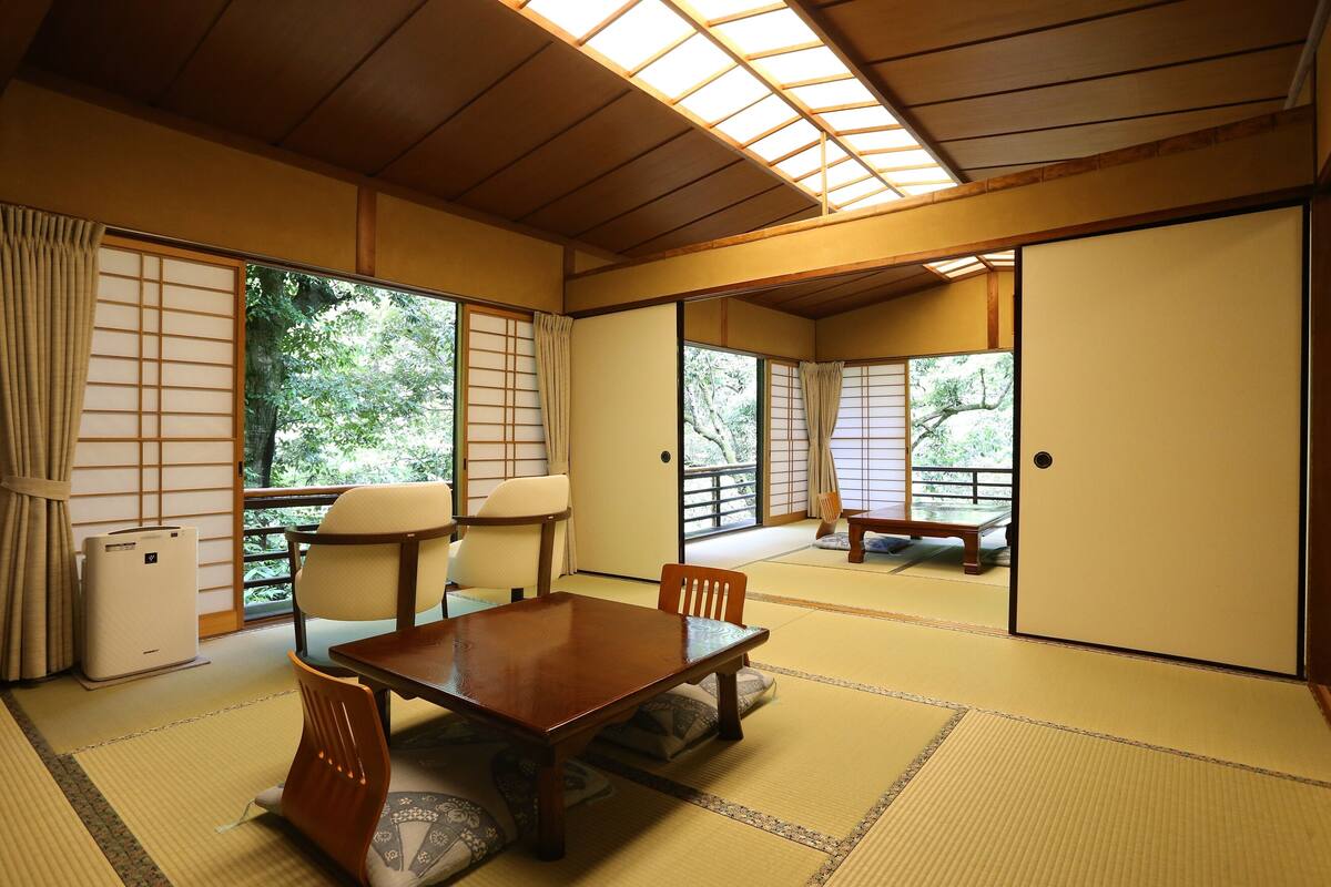 A traditional Japanese room with tatami flooring, a wooden table, chairs, and sliding doors.