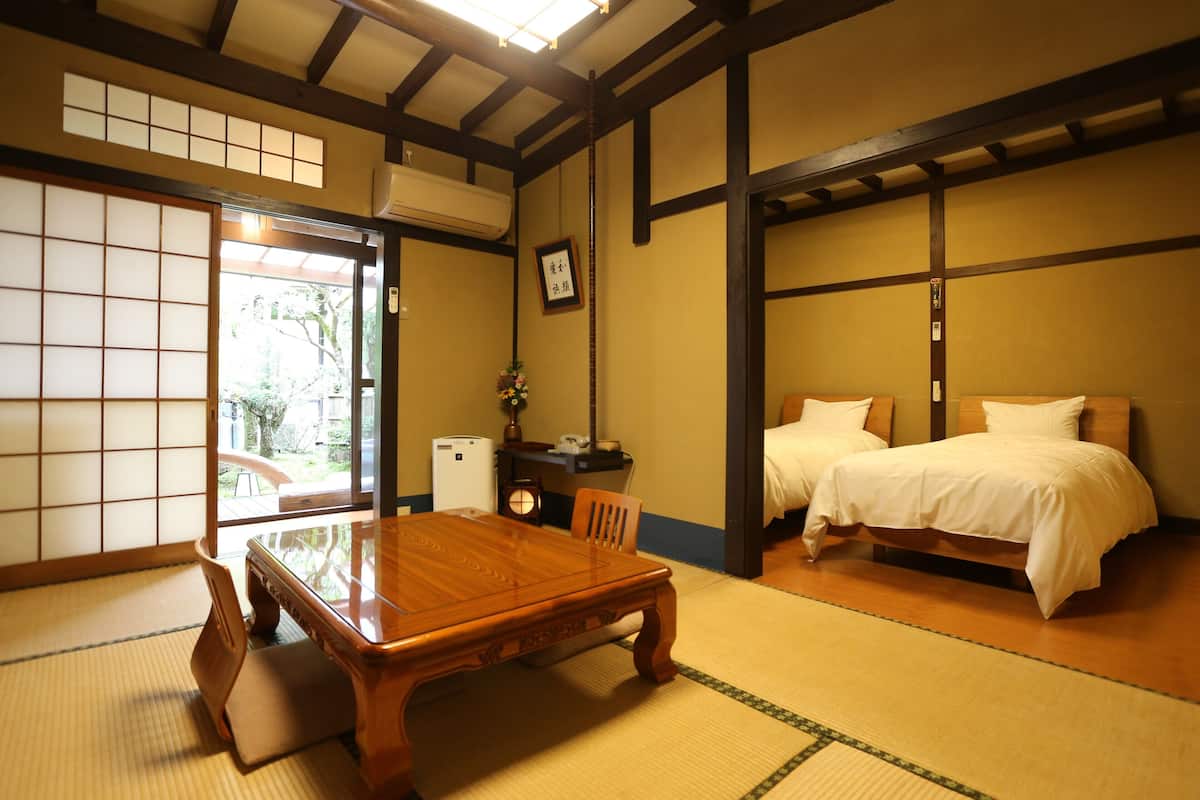 A traditional Japanese room with tatami flooring, a wooden table, two beds, and a sliding door leading to a garden.