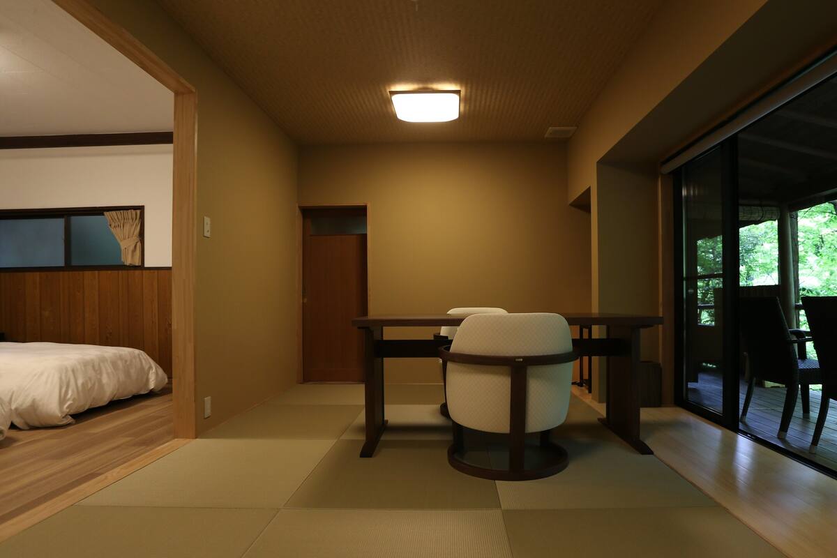 A room with a bed, a dining table with chairs, and a sliding glass door leading to an outdoor area.