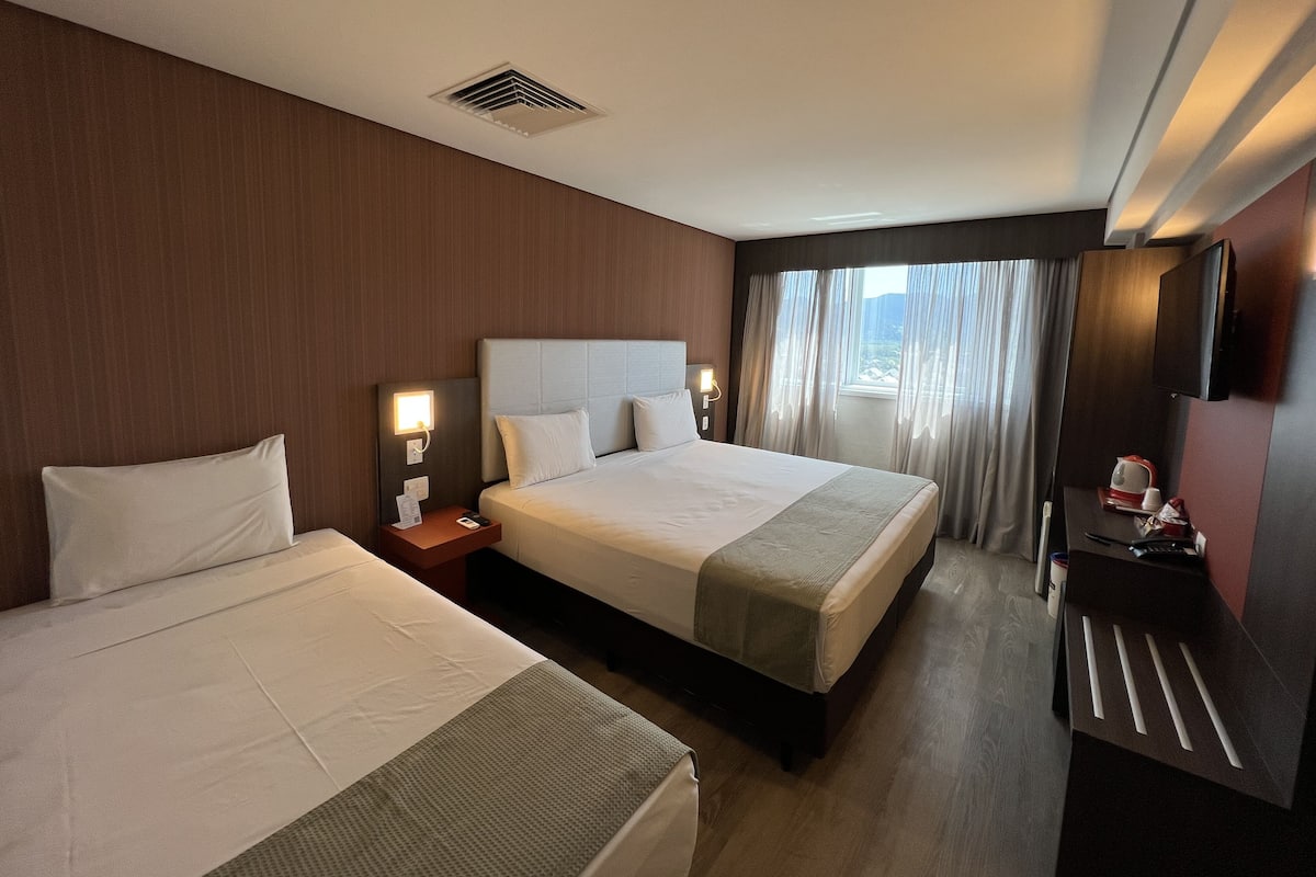 Habitación de hotel con dos camas, un escritorio con silla, televisor y ventana con cortinas.