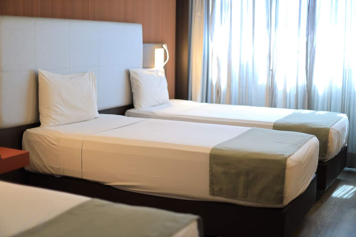 Habitación de hotel con dos camas individuales, una mesita de noche, una lámpara y una ventana con cortinas.