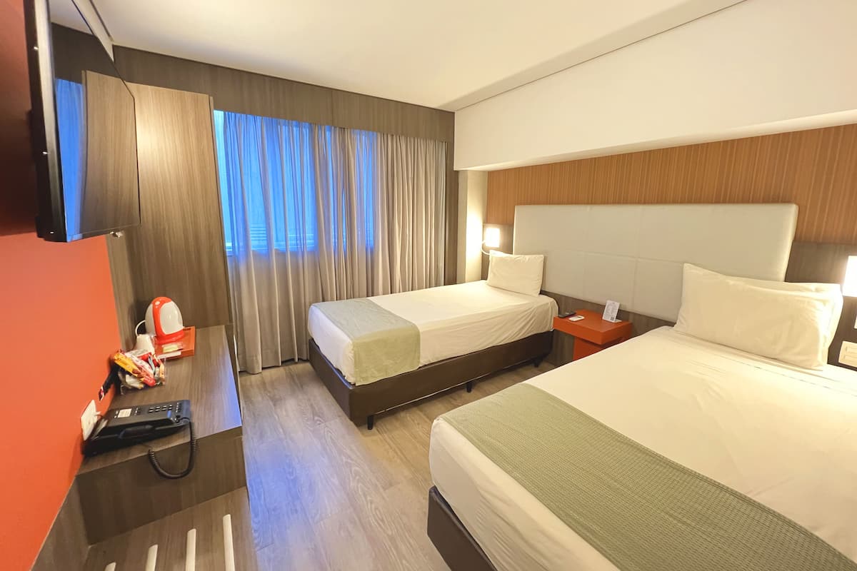 Una habitación de hotel con dos camas, un televisor, un escritorio con teléfono y una ventana con cortinas.