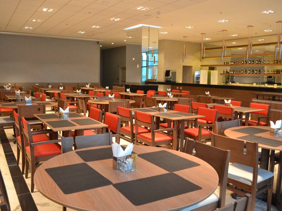 A spacious dining area with multiple tables and chairs, a bar with a variety of bottles, and a large window providing natural light.