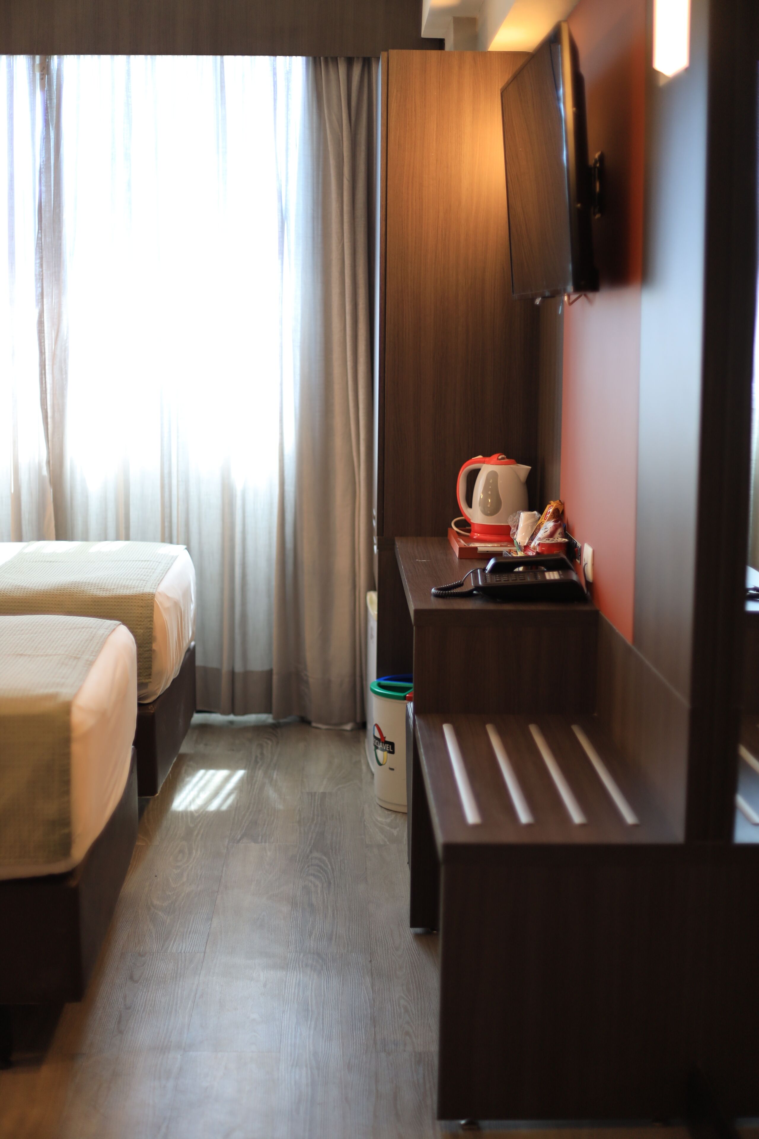 A hotel room with two beds, a desk with a telephone, a kettle, and a cup.