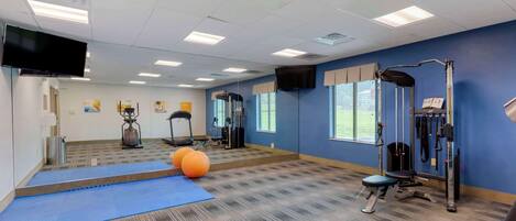 Une salle de sport équipée de matériel d’exercice, avec un tapis bleu et un téléviseur fixé au mur.