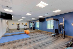 Uma academia com equipamentos de ginástica, um colchonete azul e uma televisão na parede.
