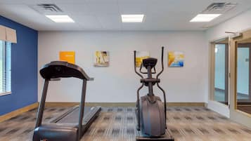 A fitness room with treadmills and an elliptical machine, a blue wall, and motivational posters.