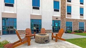 A building with a fire pit and wooden chairs in front.