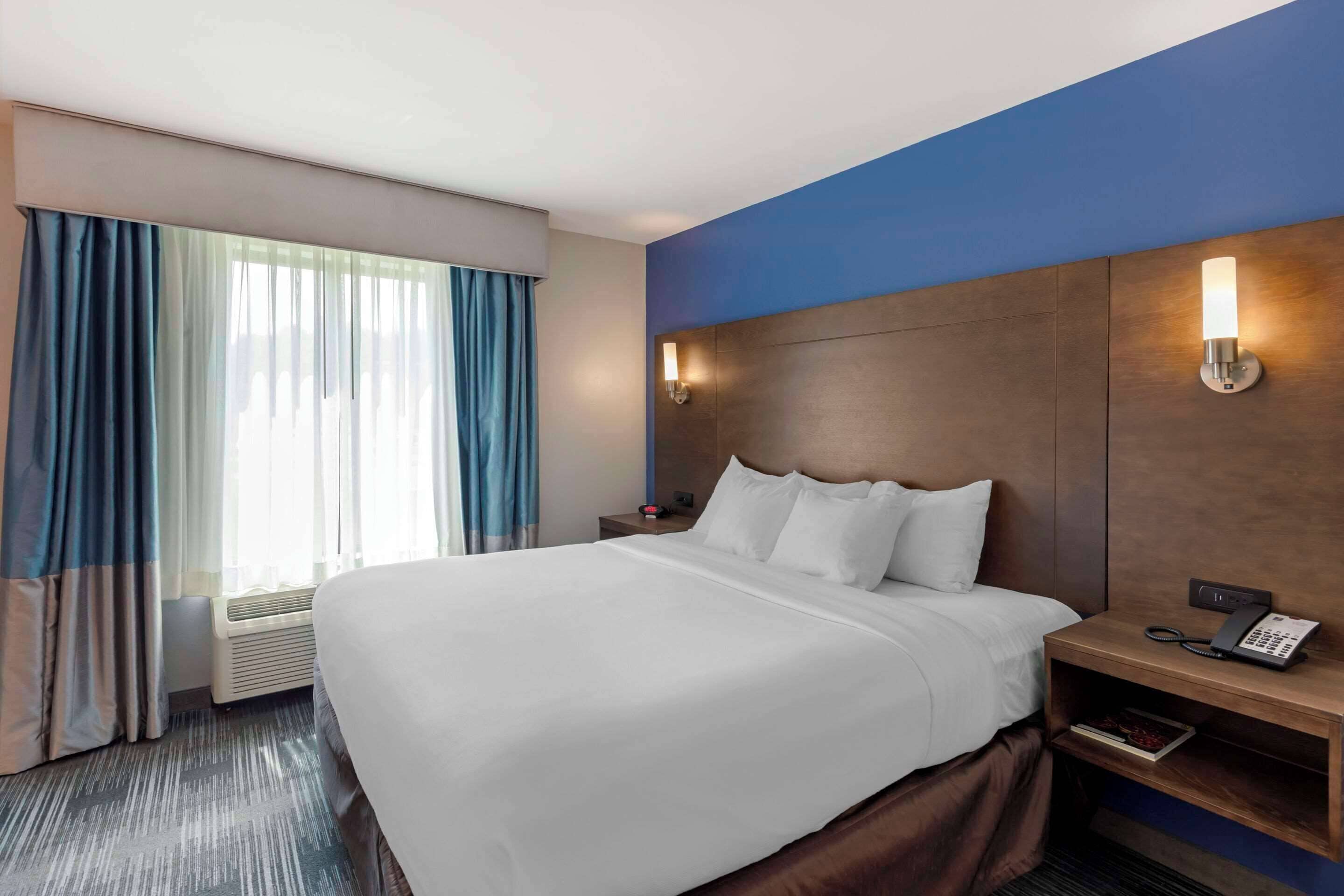 A hotel room with a large bed, a bedside table with a phone, and a window with curtains.