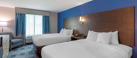 Een hotelkamer met twee bedden, een bureau, een stoel en een raam met gordijnen.