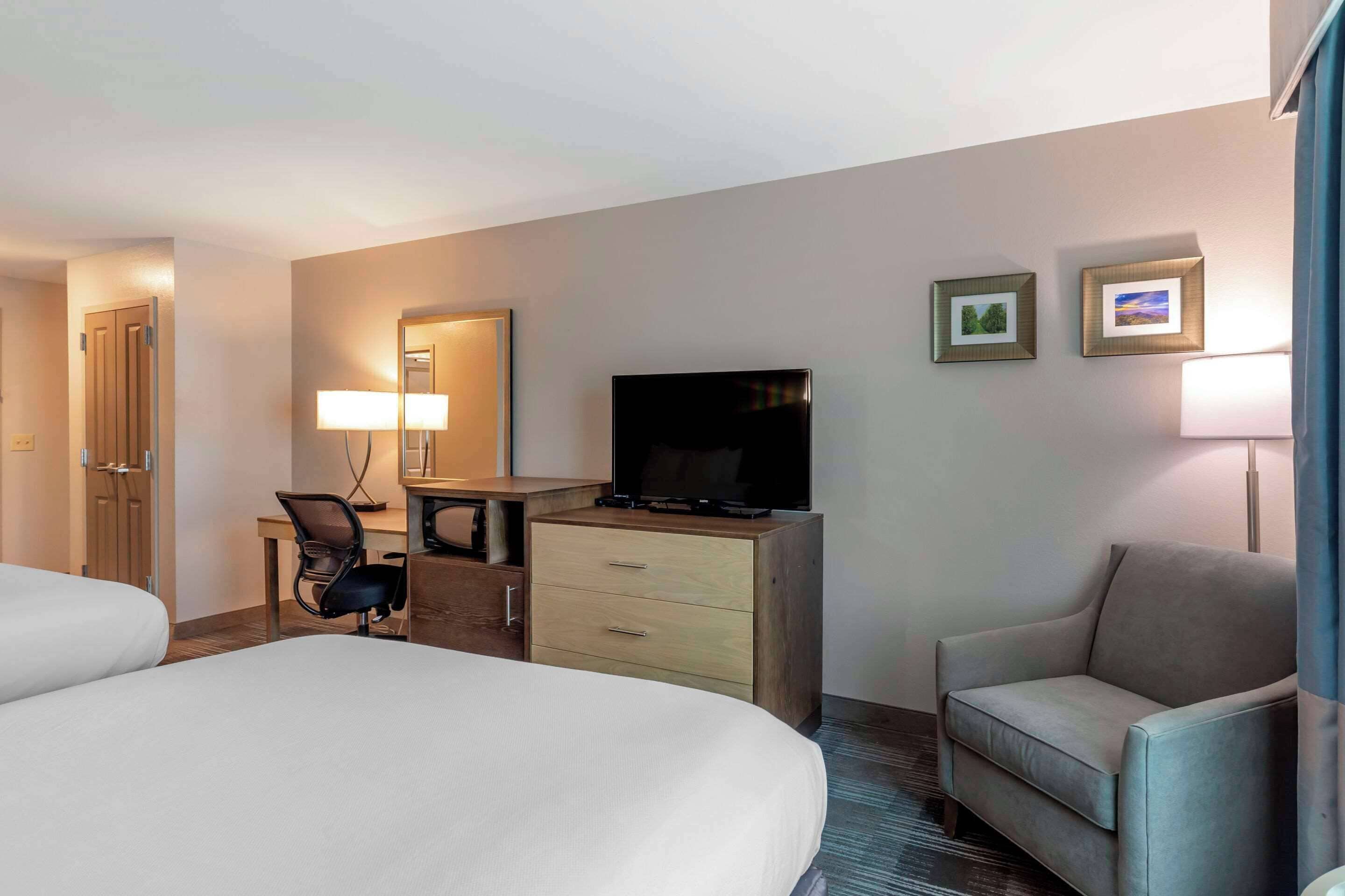 Habitación de hotel con cama, escritorio con silla, televisor y dos cuadros en la pared.