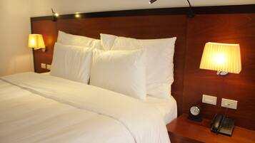 A hotel room with a large bed, two bedside lamps, a nightstand with a telephone and a clock.