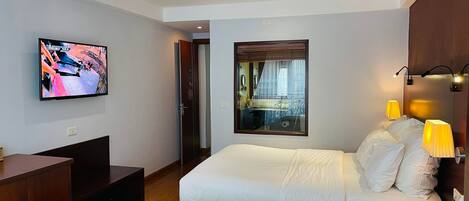 Habitación de hotel con dos camas, televisión, espejo y lámpara de noche.