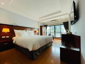 Une chambre d’hôtel avec un grand lit, des lampes de chevet, un téléviseur à écran plat, un bureau et un balcon avec vue.