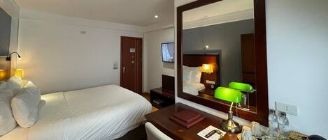 A hotel room with a bed, a desk with a lamp, a chair, a TV, and a mirror.