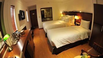 A hotel room with two beds, a desk with a lamp, and a chair.