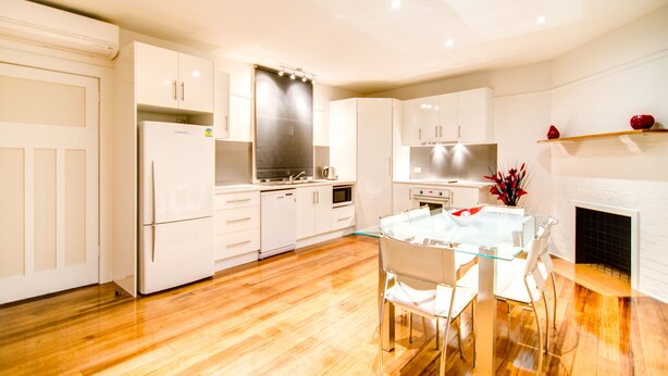 A modern kitchen with white cabinets, a glass dining table, and a fireplace. - Terrace on York (Launceston)