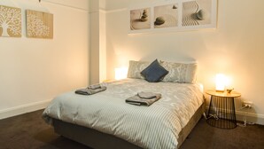 A neatly made bed with a striped blanket and pillows, a bedside table with a lamp, and wall art above the bed. - Terrace on York (Launceston)