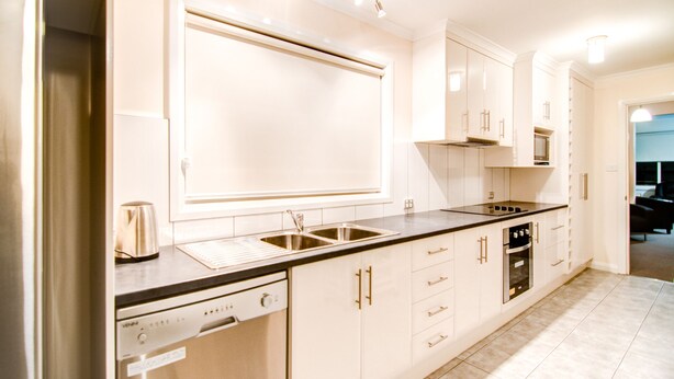 A modern kitchen with white cabinets, stainless steel appliances, and a black countertop. - Terrace on Walbourne (Launceston)