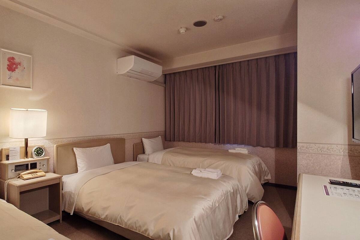 Een hotelkamer met twee bedden, een bureau, een telefoon, een airconditioner en een televisietoestel.