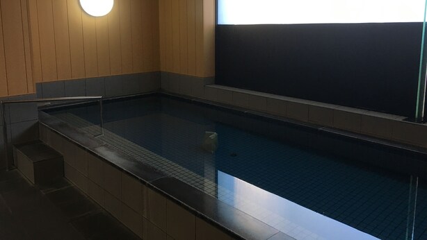 Une piscine avec un sol carrelé et un mur en bois agrémenté d’un luminaire rond.
