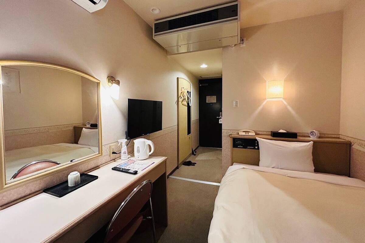 Een hotelkamer met een bed, een bureau met een spiegel, een televisie en een wandlamp.