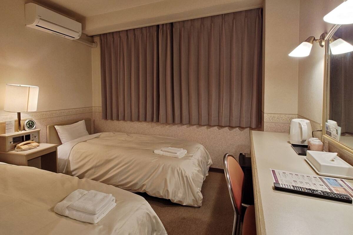 Een hotelkamer met twee bedden, een bureau, een stoel, een lamp, een klok, een spiegel en een airconditioning.