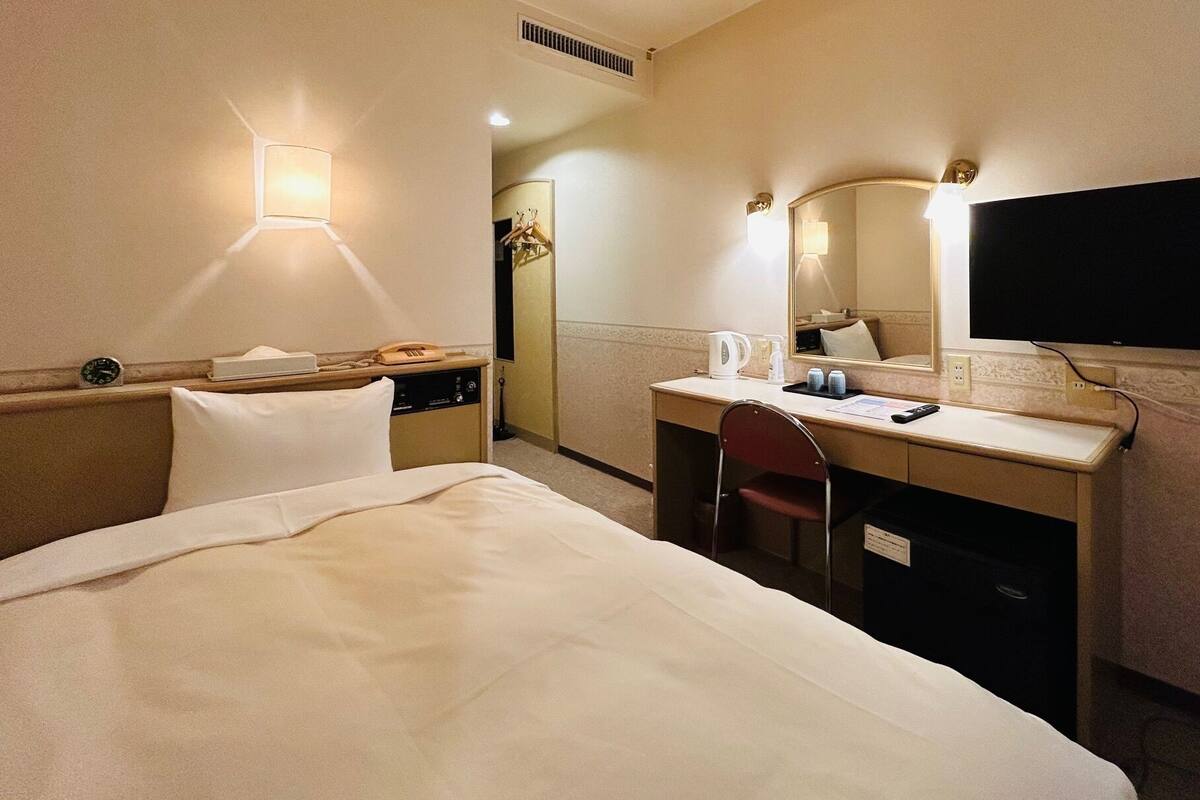 Een hotelkamer met een bed, een bureau met stoel, een televisie en een spiegel.