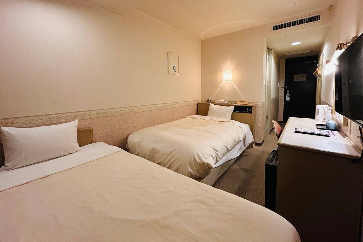 Een hotelkamer met twee bedden, een bureau met een lamp en een deur naar een andere kamer.