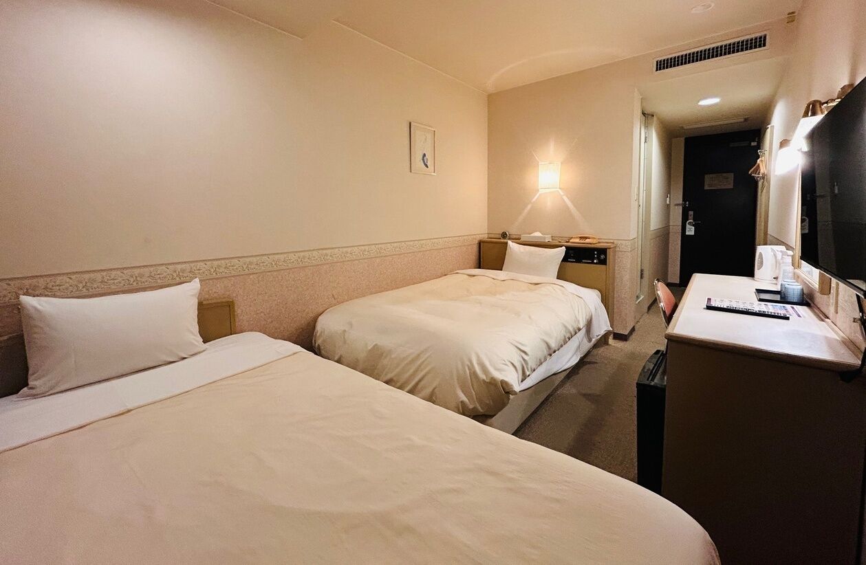 Une chambre d’hôtel avec deux lits, un bureau, une lampe et un téléviseur.
