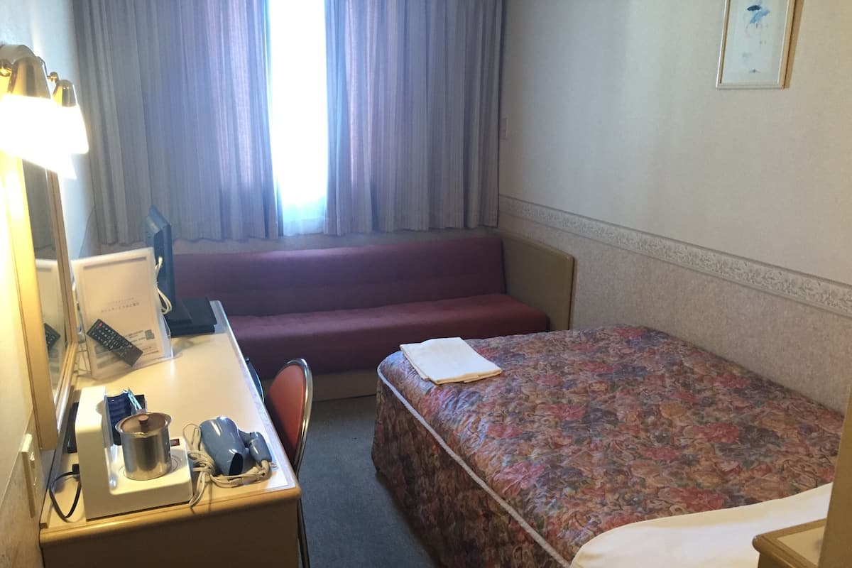 Habitación de hotel con cama, escritorio con lámpara, sillón, sofá y ventana con cortinas.