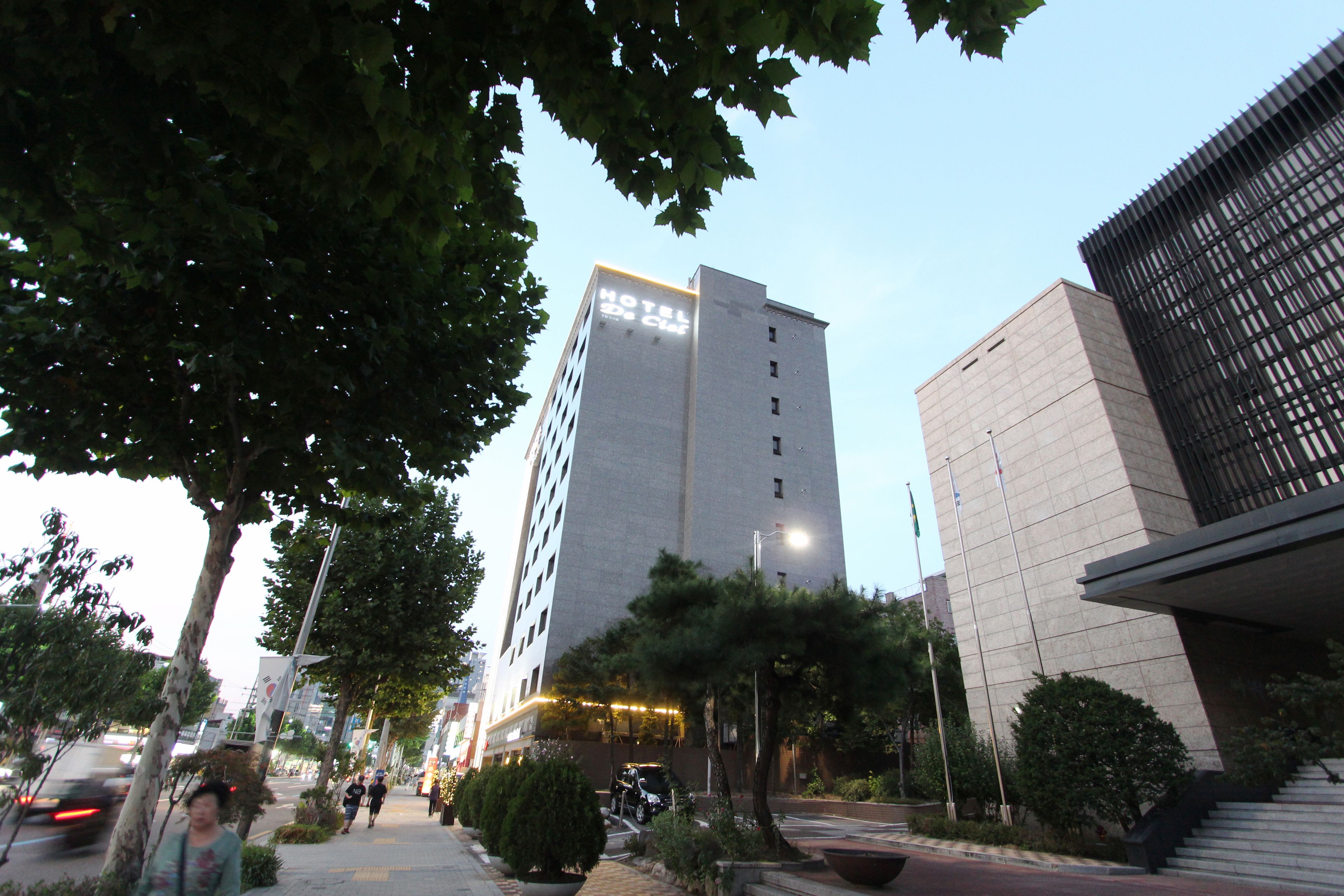 A modern hotel with a prominent sign, surrounded by trees and a well-maintained sidewalk.