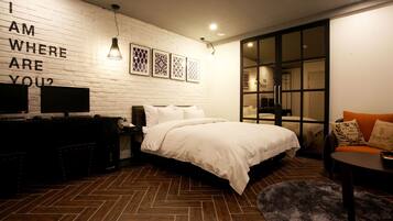 A modern bedroom with a herringbone wood floor, a large bed with white bedding, a desk with a computer, and a wall-mounted TV.