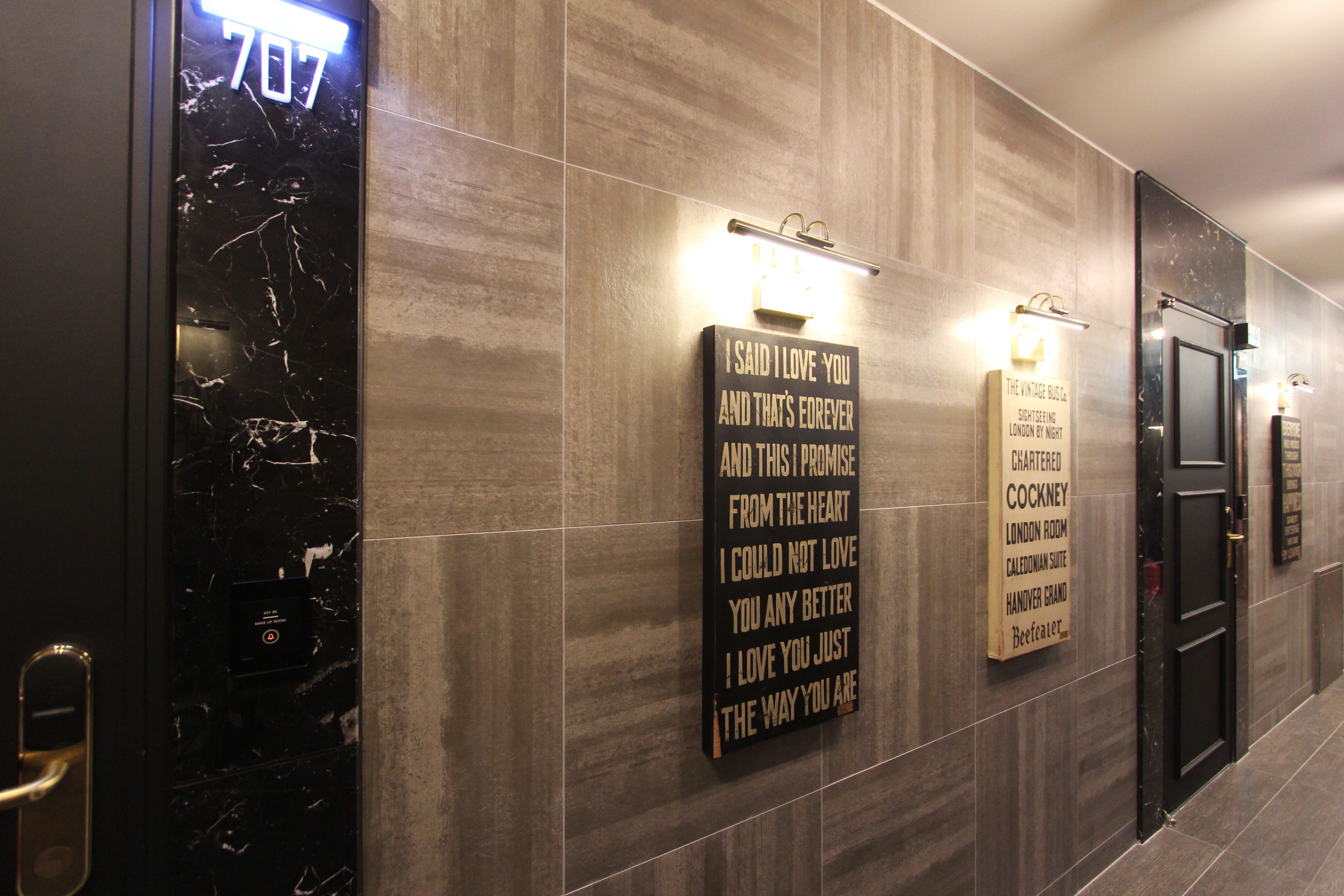 A hotel corridor with a marble wall, a sign with a love quote, and a door labeled "707".
