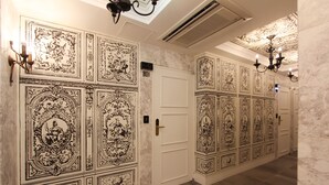 Un couloir orné de panneaux muraux noirs et blancs, une porte blanche portant un numéro et un lustre.